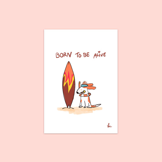 cocker qui souffle dans un tubas avec une bouée autour du cou assis sur du sable à côté d'une planche de surf. il y a écrit à la main "born to ve alive". 